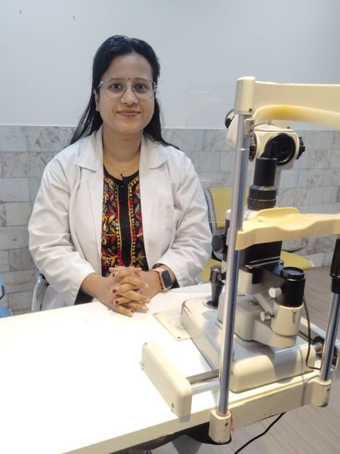Dr. Drishti Kumari in a white coat, seated beside a slit lamp